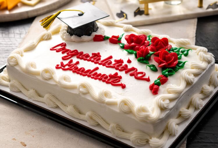 Graduation sheet cake with white frosting, red piped "Congratulations Graduate" text, red frosting roses, and a miniature black graduation cap topper.